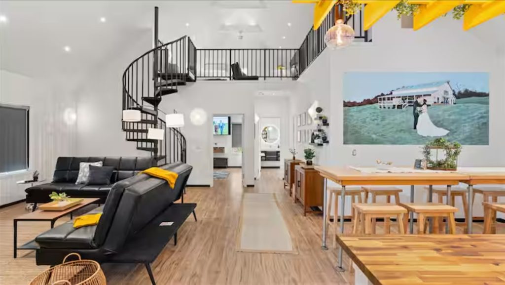 Modern loft interior with spiral staircase, black furniture, wooden dining table, and wedding photo on wall.