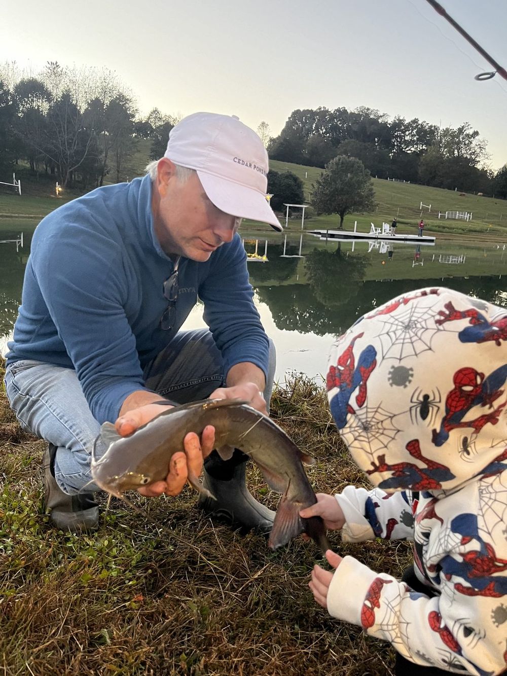A farm guide holding a catfish while a child in a hooded sweatshirt touches it